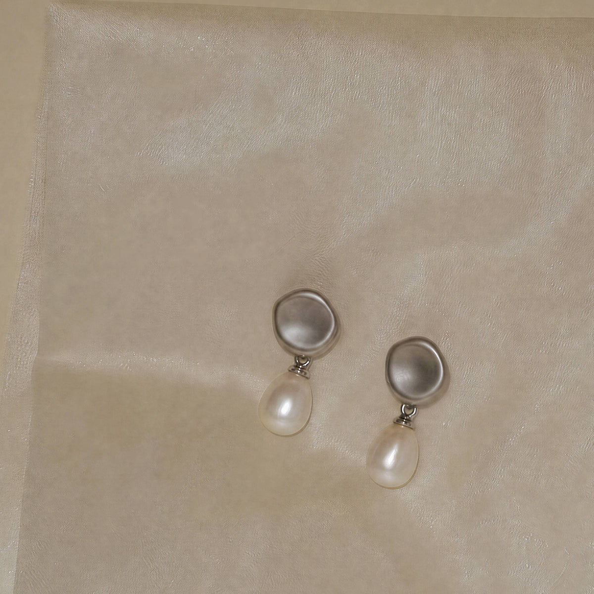 Minimal silver pearl earrings resting on textured surface, Falling Dew by ORIN