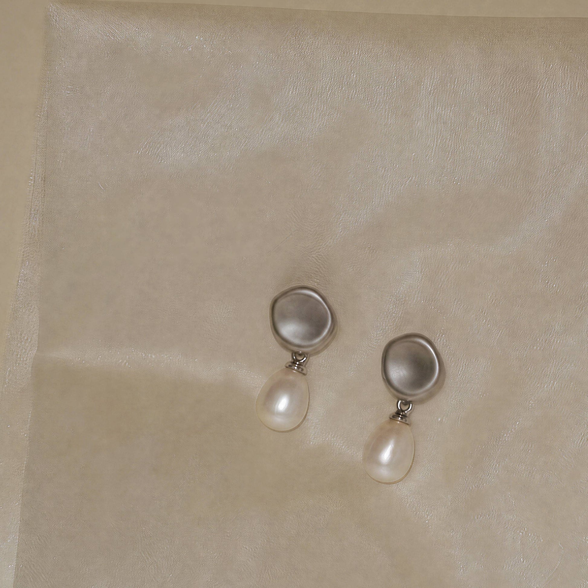 Minimal silver pearl earrings resting on textured surface, Falling Dew by ORIN