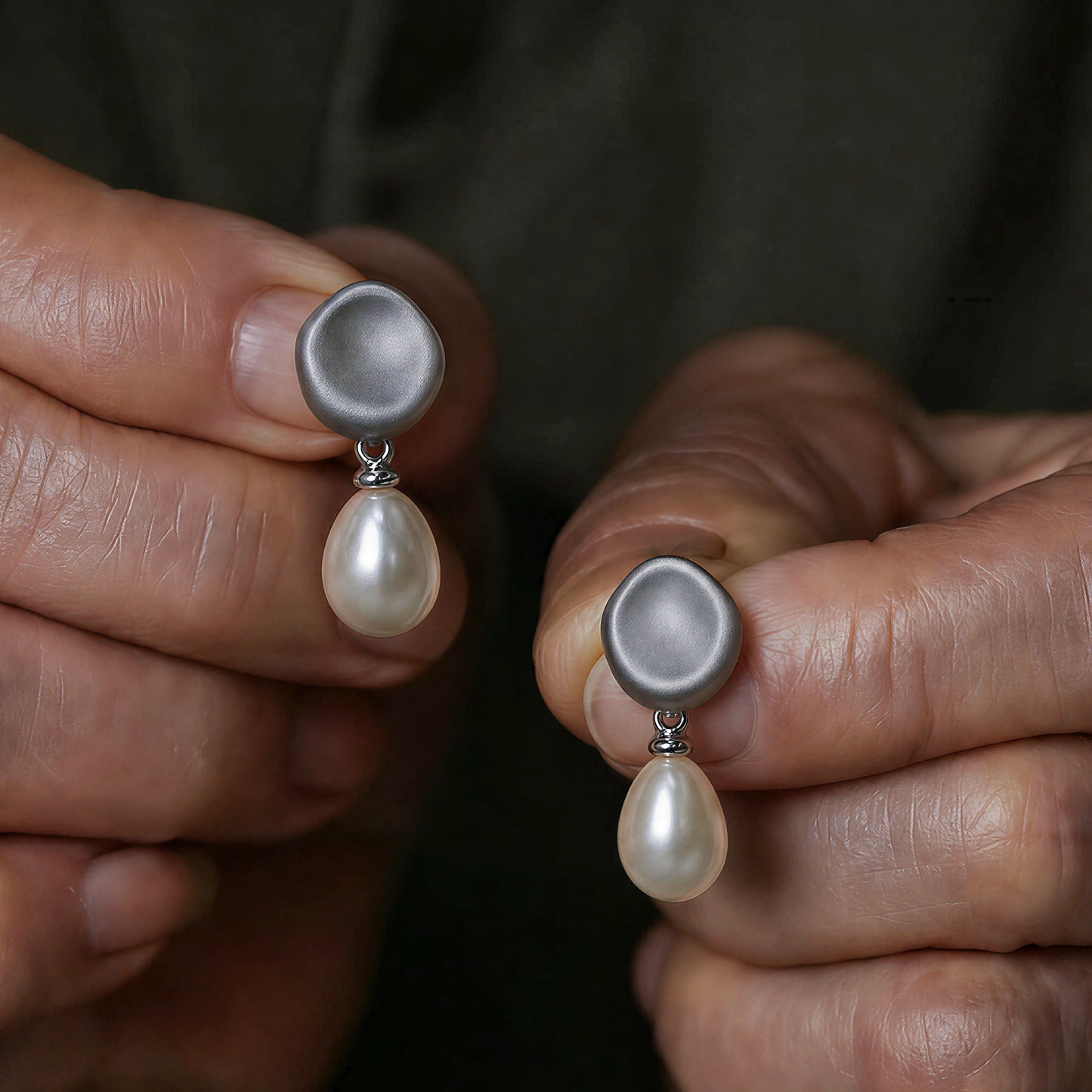 Hand holding Falling Dew silver pearl earrings showing organic silver form