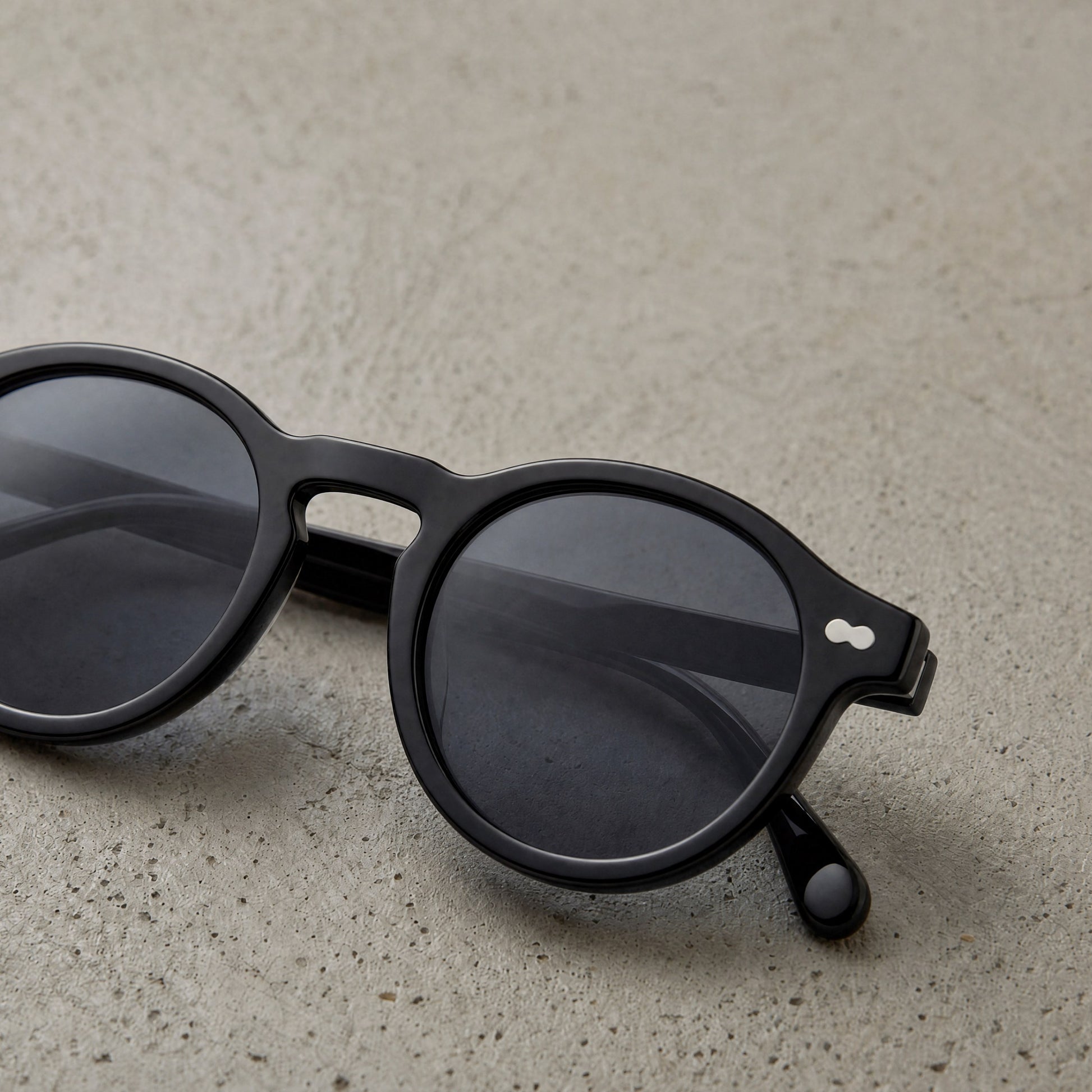 Black round acetate sunglasses resting on textured stone surface