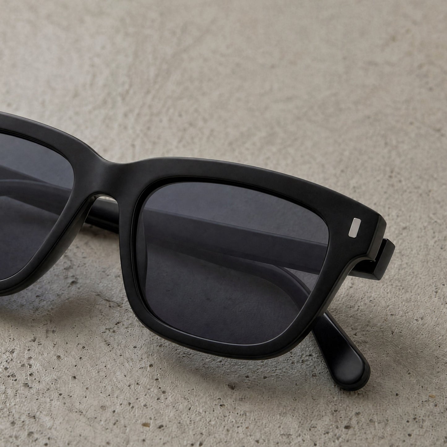 Close-up of Pine Shade square sunglasses resting on textured stone surface