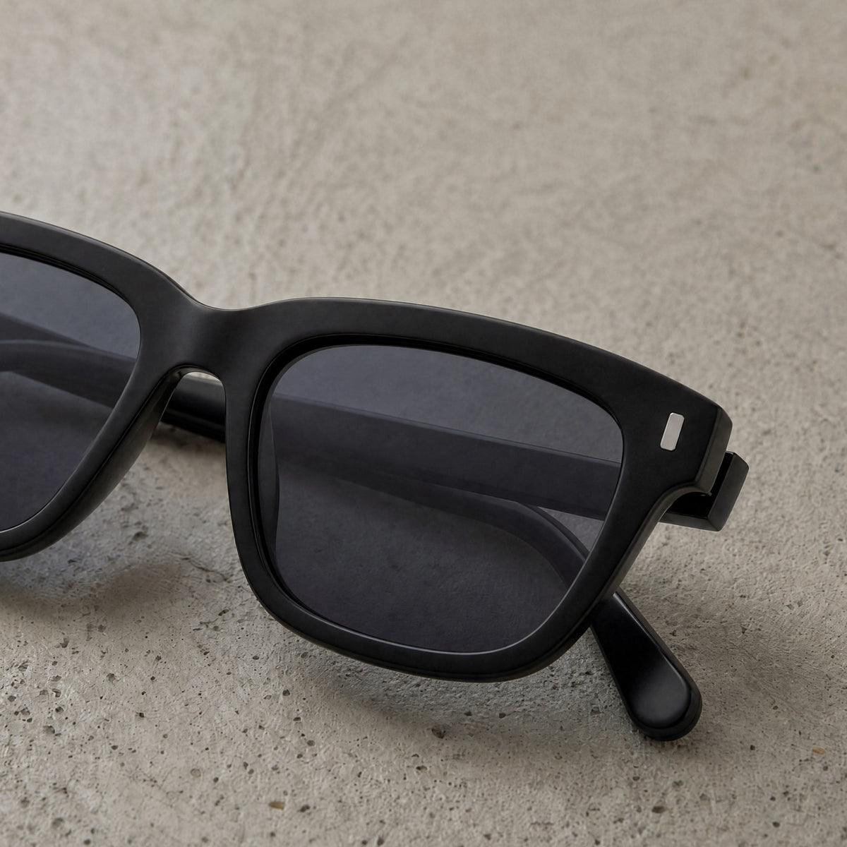 Close-up of Pine Shade square sunglasses resting on textured stone surface