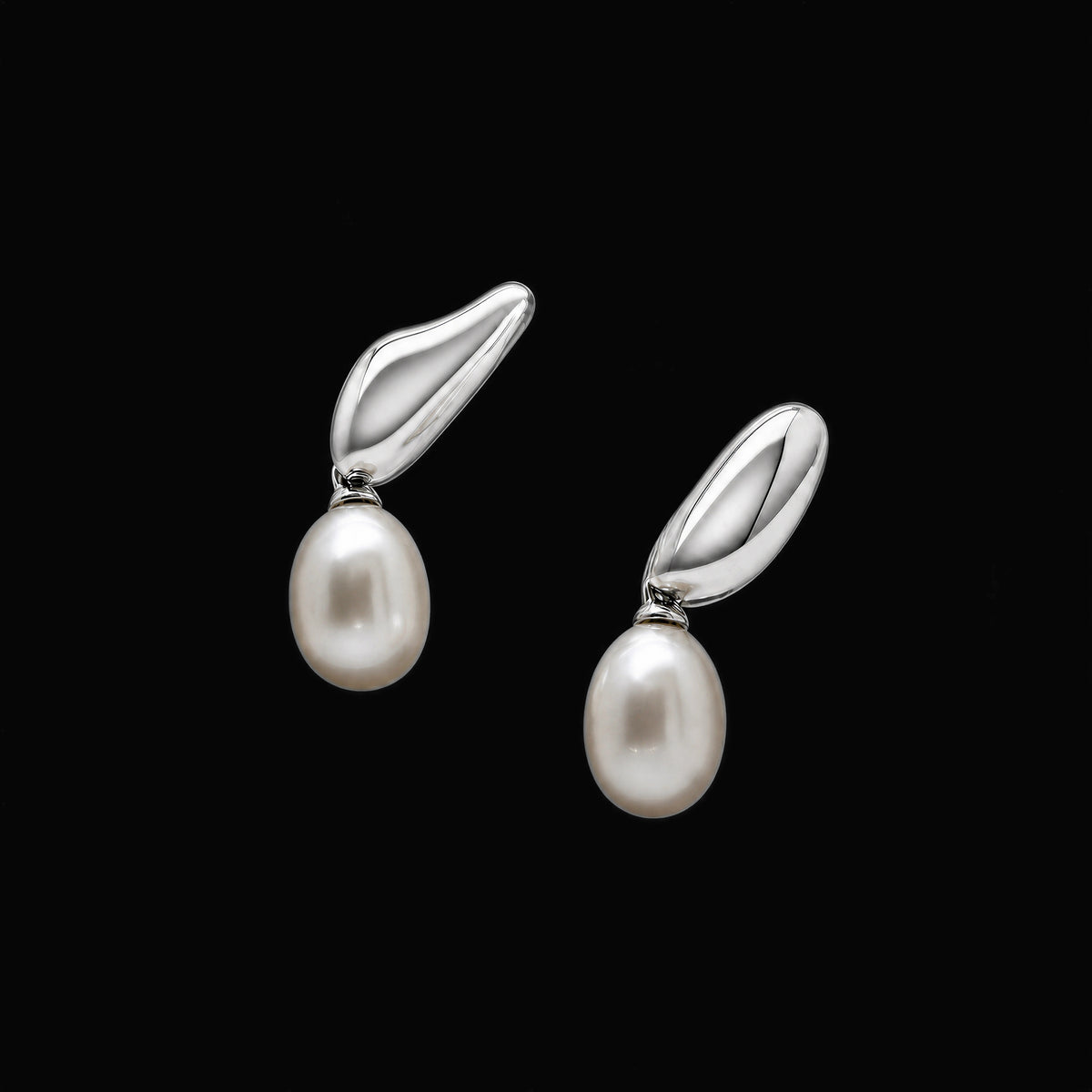 Silver pearl drop earrings on a black background, featuring sculptural sterling silver forms and freshwater pearls.